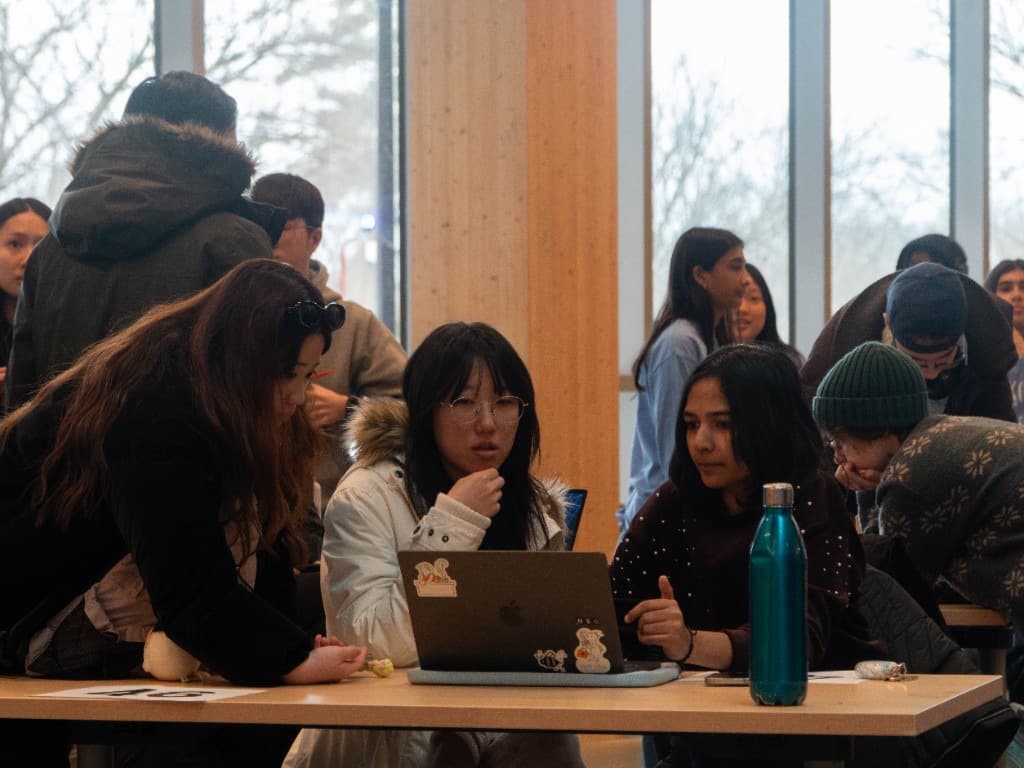 Three students focused on a laptop screen while collaborating at their table.