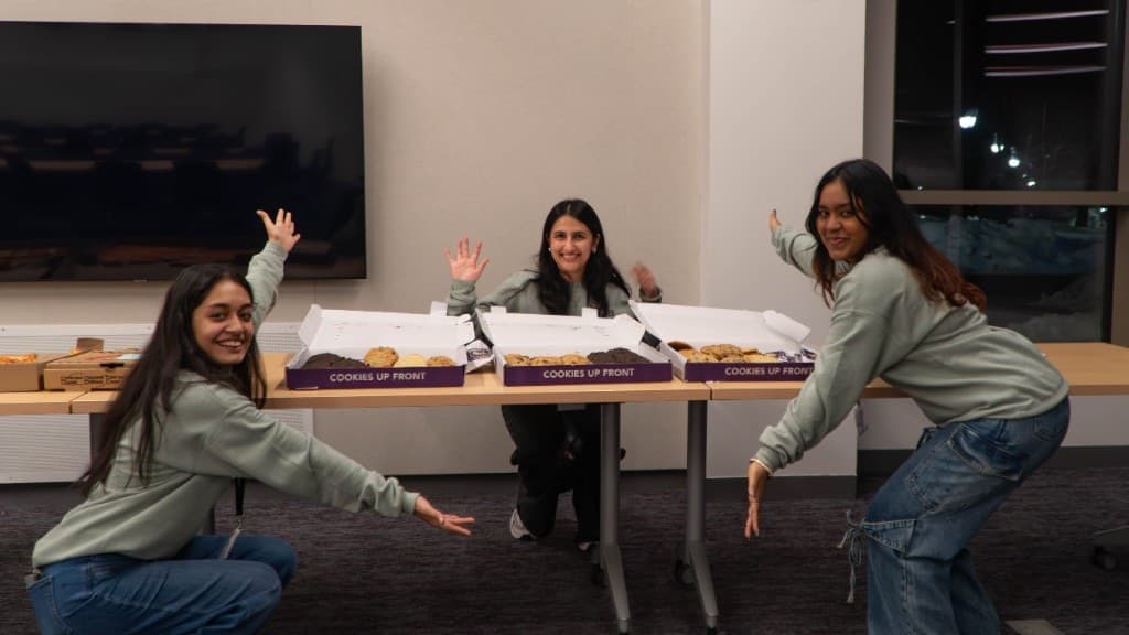 Three organizers in green sweatshirts celebrating open boxes of cookies at the snack table.