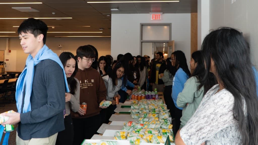 Attendees gathering around a long table of sandwiches and drinks during a meal break.