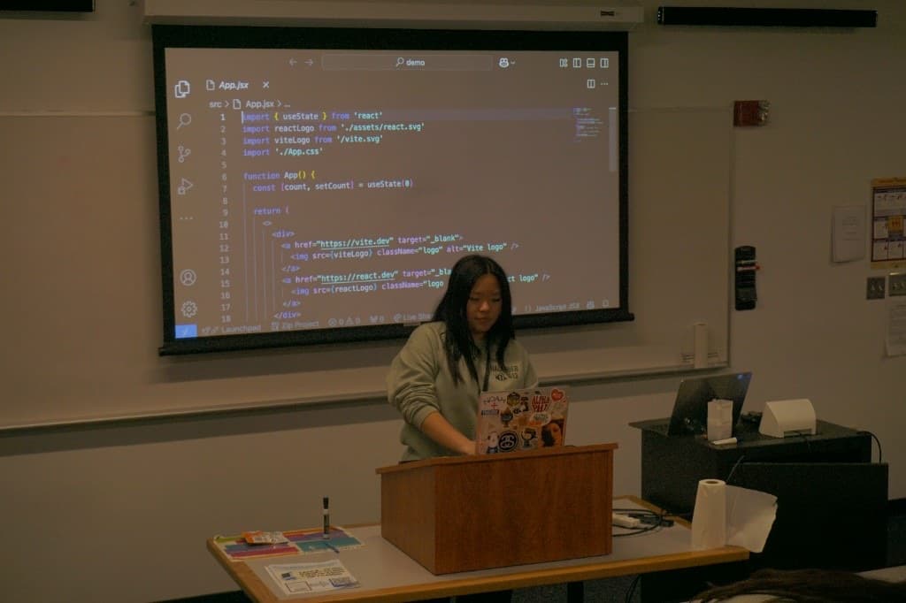 A student presenting a React demo from a podium with code projected behind them.